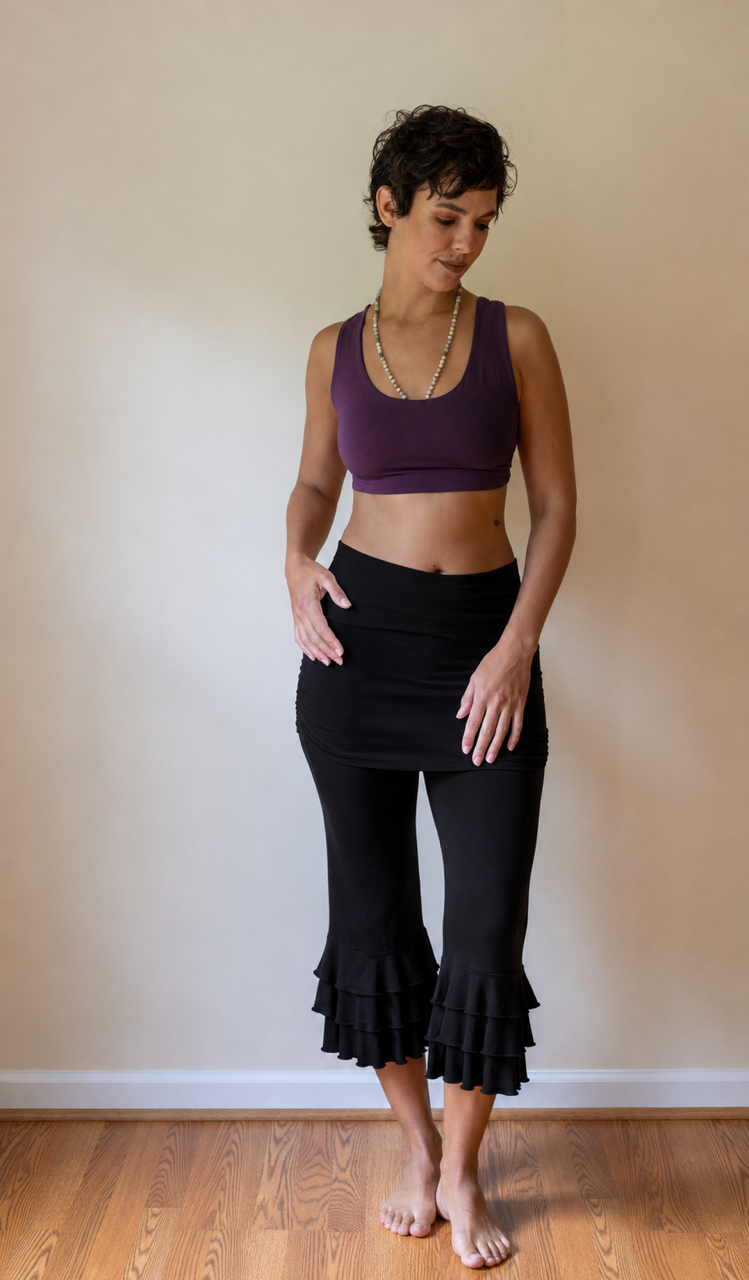 Woman wearing a purple sports bra and black capri pants standing against a plain wall.