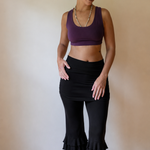 Woman wearing a purple sports bra and black capri pants standing against a plain wall.